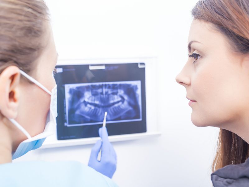 Odontóloga mostrando resultados de examen de odontología digital a paciente femenina con vista a imagen digitalizada de su dentadura en una pantalla