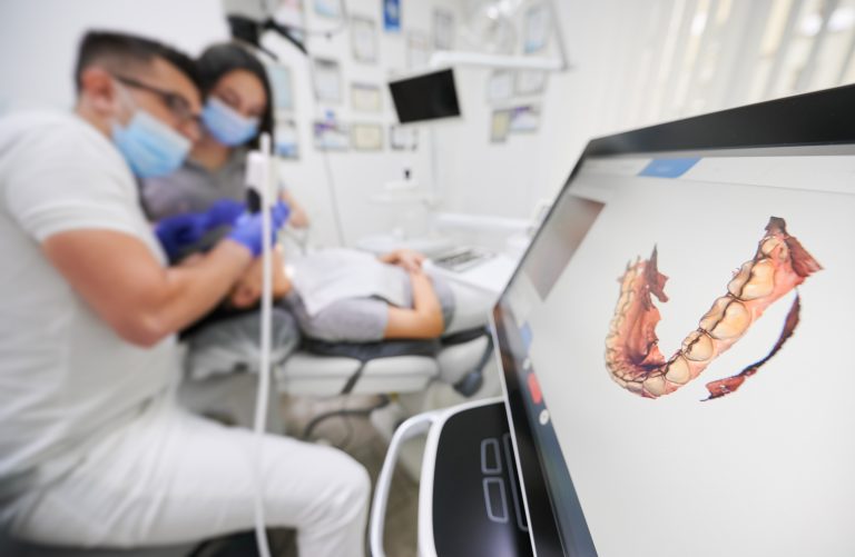 Odontólogo y técnico médico realizando procedimiento de odontología digital en un paciente con vista a imagen digitalizada de su dentadura en una pantalla