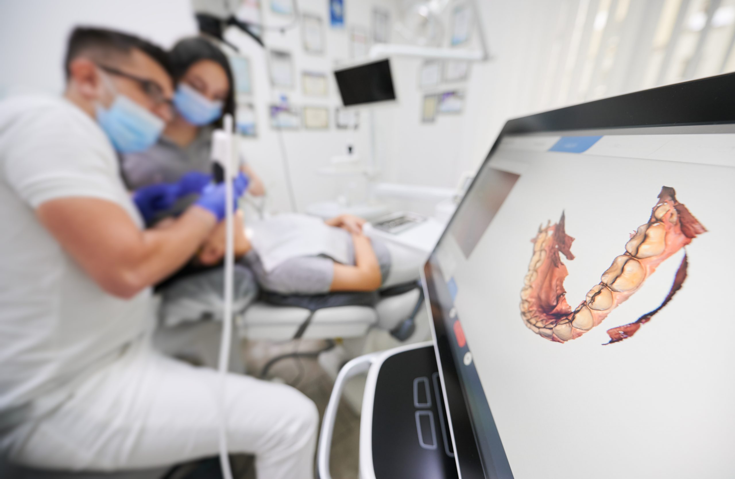 Odontólogo y técnico médico realizando procedimiento de odontología digital en un paciente con vista a imagen digitalizada de su dentadura en una pantalla