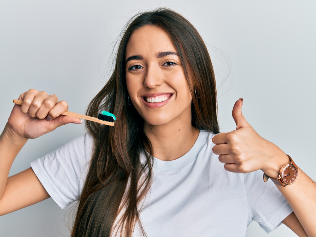 mujer joven sosteniendo cepillo de dientes con pasta dental. Está sonriendo y con el pulgar arriba en señal de aprobación