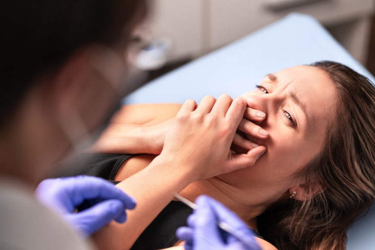 mujer sobre una camilla en box dental cubriéndose la boca con las manos expresando miedo al dentista