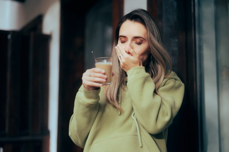 mujer con sensibilidad en los dientes. Se cubre la boca con la mano al sentir dolor por beber una leche fría.