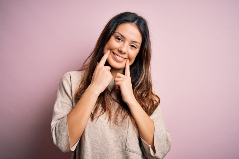 mujer sonriente con sus dedos guiando una sonrisa alegre gracias a tratamientos dentales