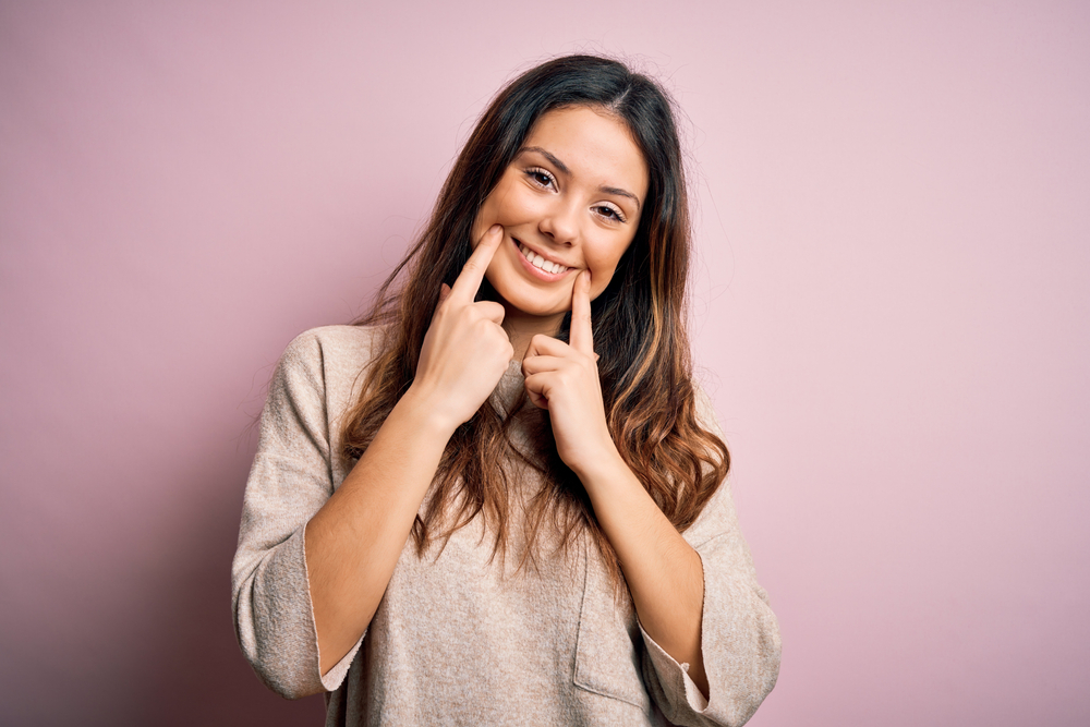 mujer sonriente con sus dedos guiando una sonrisa alegre gracias a tratamientos dentales