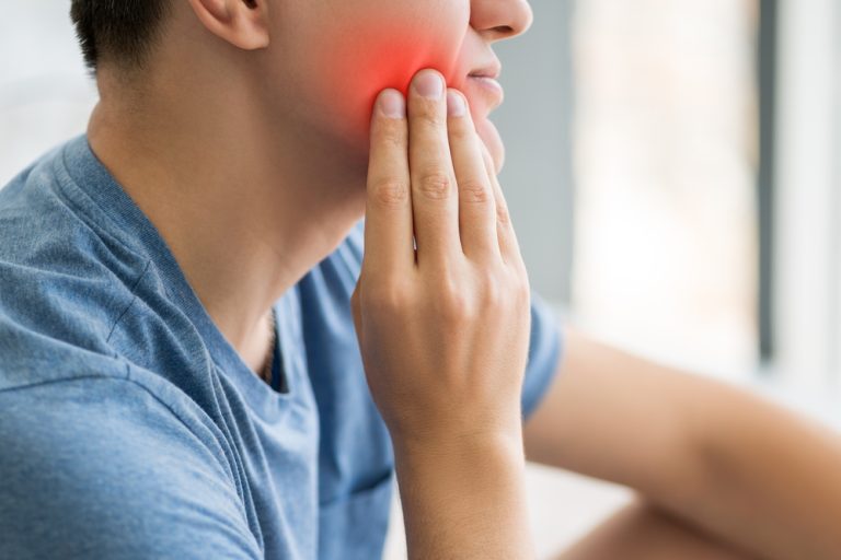 hombre tocándose una mejilla con dolor dental por enfermedad periodontal