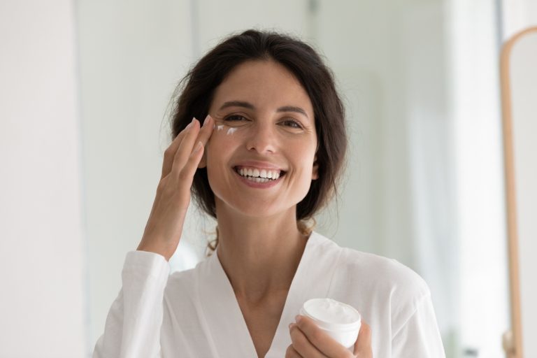 mujer feliz aplicándose crema para un rostro natural