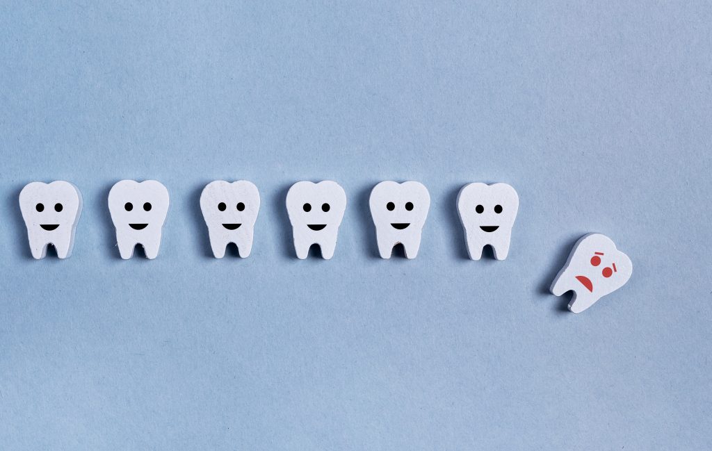 Imagen alegórica del por qué se caen los dientes donde se muestra una hilera de dientes con carita feliz y un diente con cara triste cayendo a un costado